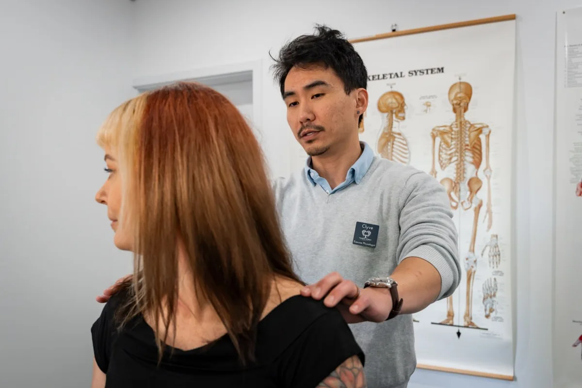 Clyve Tan assessing a patient's shoulder movement against the skeletal chart in his room