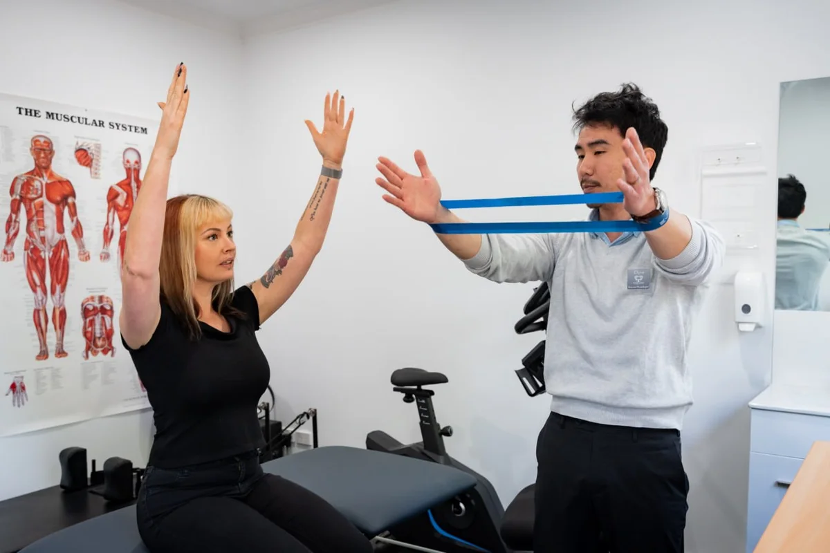 Clyve Tan guiding a patient through a resistance band exercise in the exercise physiology room at Thorpe Street Health