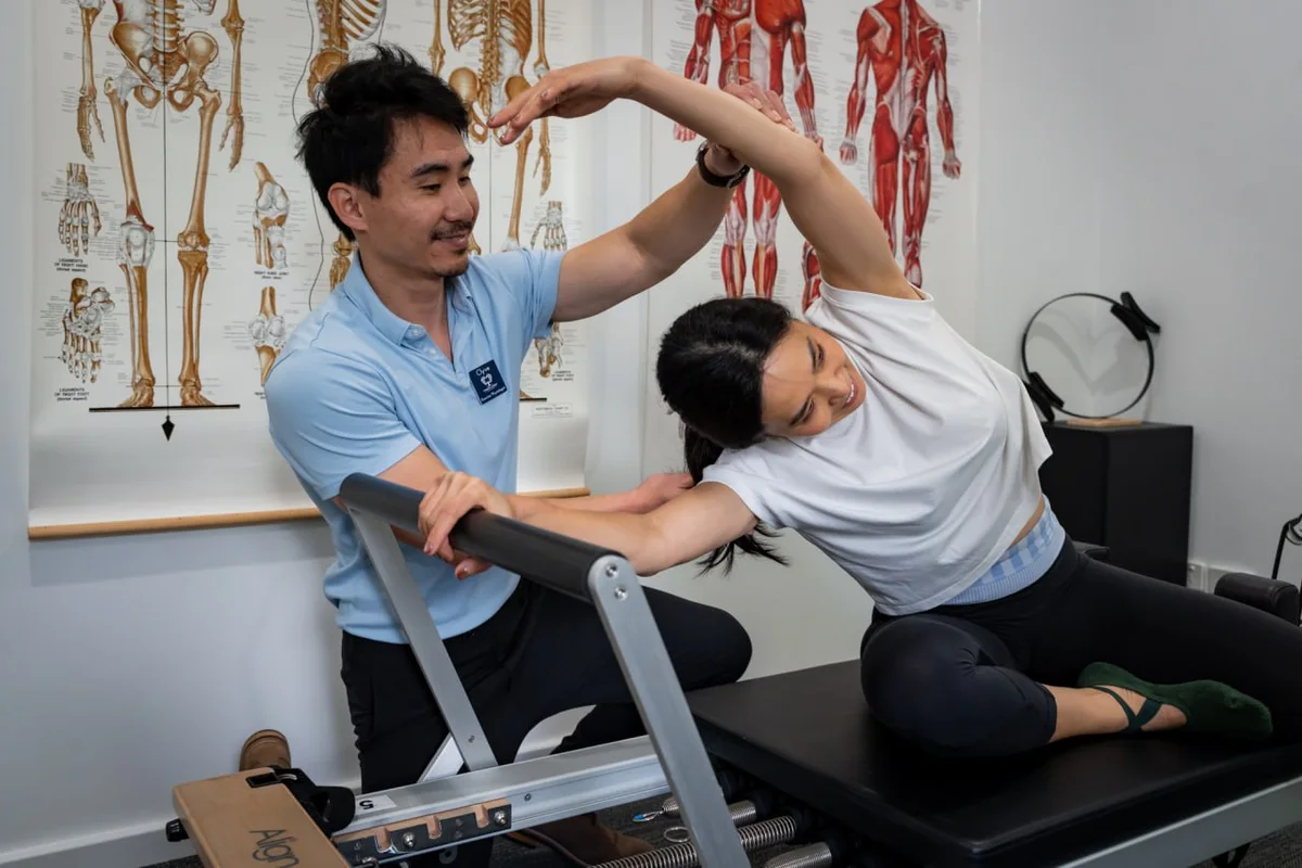 Clyve Tan supporting a patient through a stretch on the clinical reformer